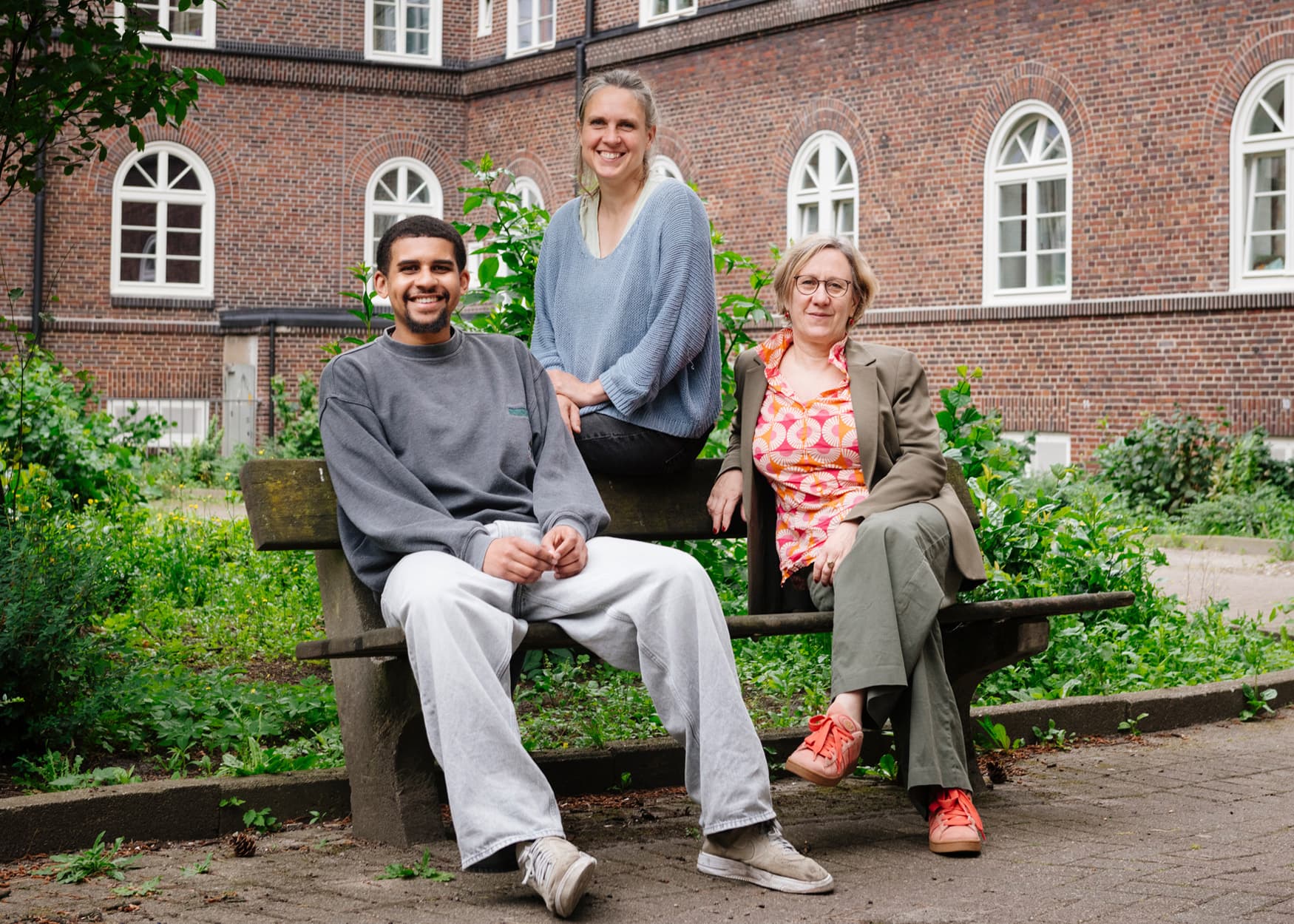 Koordinationsteam des CHL auf einer Bank vor einem Backsteinhaus. Von links nach rechts: Ebou Saine Uhlig, Anna Köster-Eiserfunke, Silke Betscher.